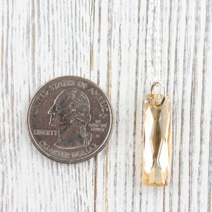 May include: A gold-toned crystal pendant hangs from a silver chain. The pendant is rectangular and faceted, and it is about the size of a UK 20 pence coin.