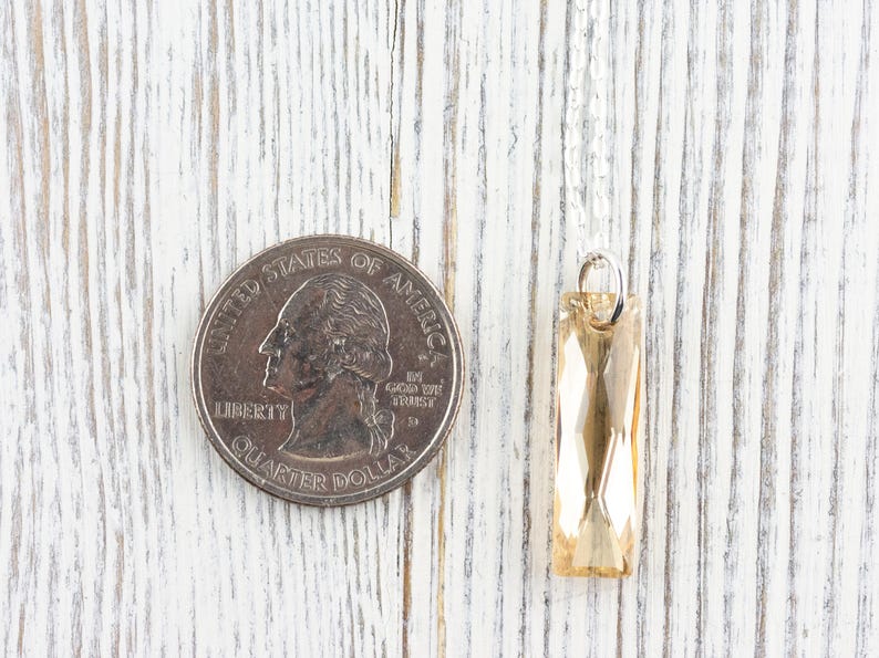 May include: A gold-toned crystal pendant hangs from a silver chain. The pendant is rectangular and faceted, and it is about the size of a UK 20 pence coin.