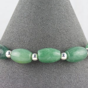 May include: A green jade stone bracelet with silver beads. The bracelet is made of oval-shaped jade stones and silver beads.