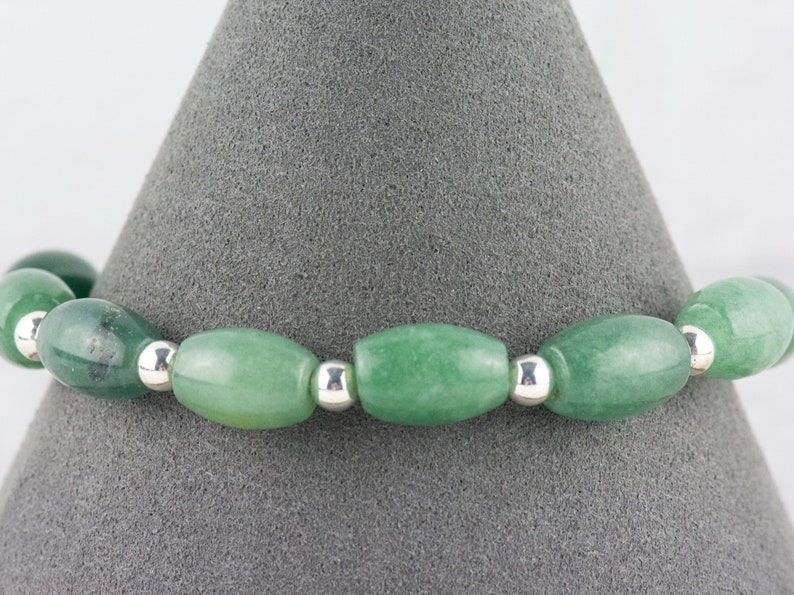 May include: A green jade stone bracelet with silver beads. The bracelet is made of oval-shaped jade stones and silver beads.