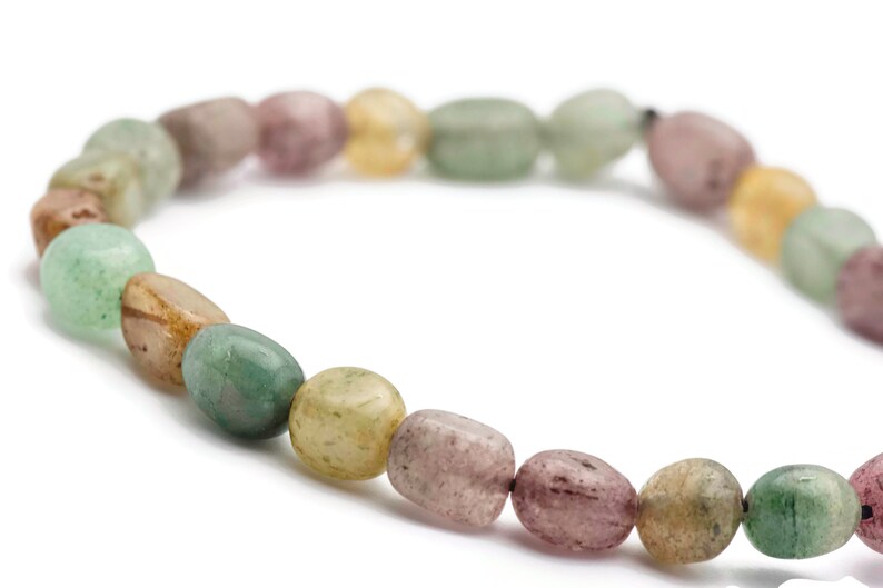 May include: A bracelet made of oval-shaped, multi-coloured gemstone beads. The beads are shades of green, brown, pink, and yellow.
