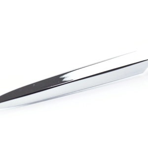May include: A shiny, silver letter opener with a sharp, pointed end. The opener has a geometric, angular design and a rounded handle. The metallic surface reflects light, creating highlights and shadows.