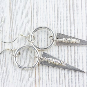 May include: Silver earrings with a circle and a triangle pendant. The triangle pendant has a row of small silver beads.