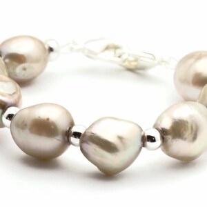 Peut inclure: Un bracelet compos&eacute; d'un brin de grosses perles grises p&acirc;les et de perles argent&eacute;es.