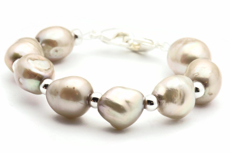 Peut inclure: Un bracelet compos&eacute; d'un brin de grosses perles grises p&acirc;les et de perles argent&eacute;es.
