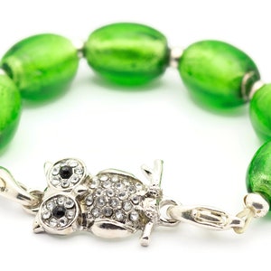 May include: A green glass bead bracelet with an owl charm. The owl charm is silver with rhinestones and black eyes.