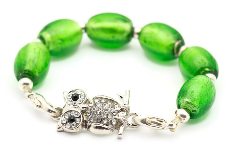 May include: A green glass bead bracelet with an owl charm. The owl charm is silver with rhinestones and black eyes.