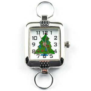 Puede incluir: Un reloj de llavero rectangular plateado con una esfera blanca con n&uacute;meros negros y un dise&ntilde;o de &aacute;rbol de Navidad verde. El reloj tiene una corona para ajustar la hora y dos llaveros.