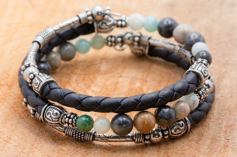 May include: A black leather bracelet with silver beads and green, brown, and gray stones.