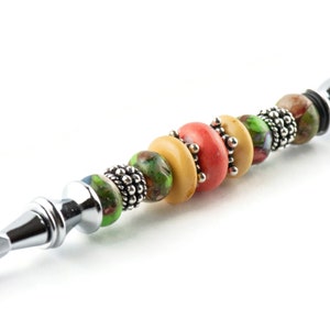 May include: A silver letter opener with a handle decorated with colourful glass beads. The beads are green, yellow and orange.