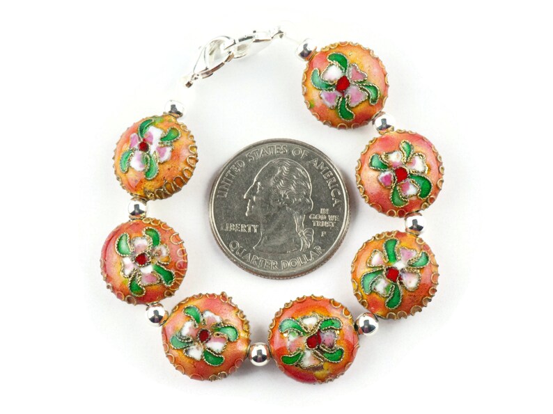 May include: A bracelet made of round, orange beads with floral designs in pink, green, and white. The beads are about the size of a US quarter. The bracelet has a silver clasp.