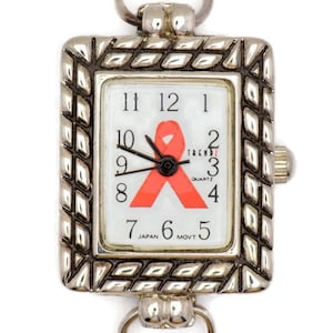 May include: A silver watch with a white face and a pink ribbon design. The watch face also has the text "TRENDZ QUARTZ JAPAN MOVT".