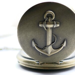 May include: A silver pocket watch with an anchor design on the front. The anchor is detailed with a rope design.