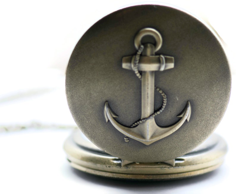 May include: A silver pocket watch with an anchor design on the front. The anchor is detailed with a rope design.