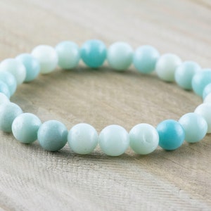 May include: A light blue and white beaded bracelet made of smooth, round stones. The bracelet is made of natural stones and has a calming, ocean-inspired colour scheme.