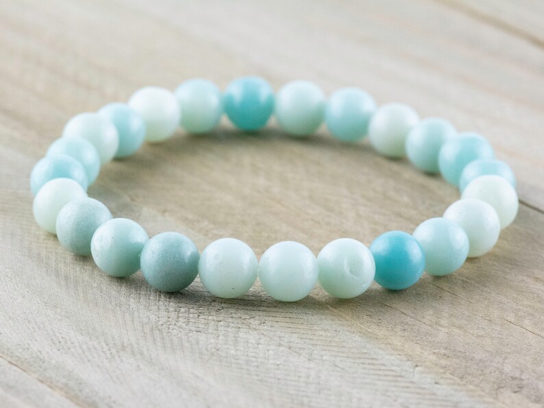 May include: A light blue and white beaded bracelet made of smooth, round stones. The bracelet is made of natural stones and has a calming, ocean-inspired colour scheme.
