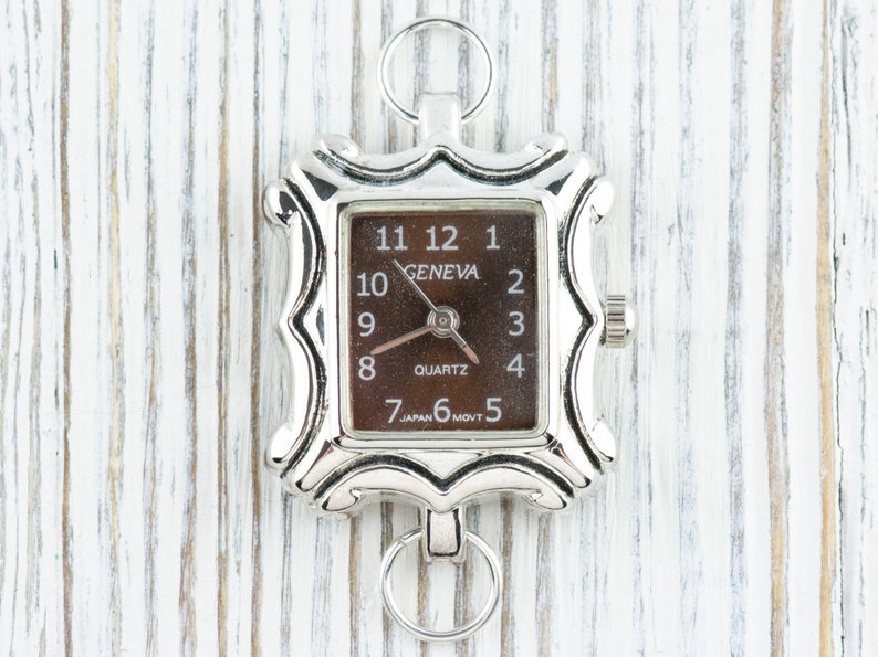 May include: A silver-toned watch with a square face and a brown dial. The watch face has black Roman numeral hour markers and the words "GENEVA" and "QUARTZ".