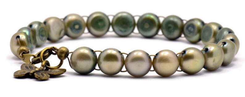 Op de afbeelding: Een armband gemaakt van groene en gouden parels met een vlinderbedel. De armband is gemaakt van draad en heeft een sluiting.
