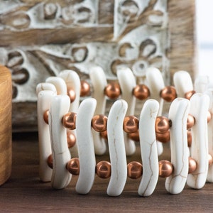 May include: A white and copper bracelet with a wavy design. The bracelet is made of white beads and copper beads.