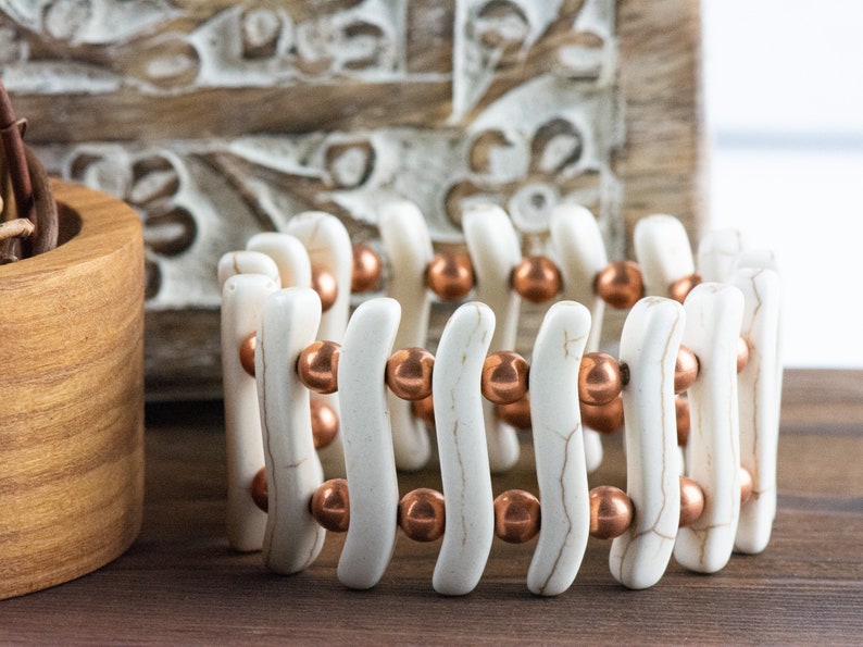 May include: A white and copper bracelet with a wavy design. The bracelet is made of white beads and copper beads.