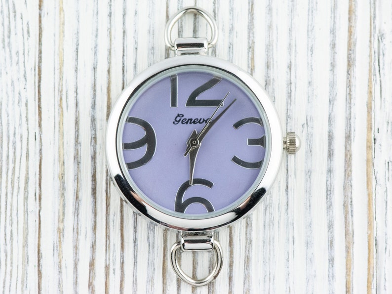 May include: A silver watch with a purple face and black numbers. The watch has a Geneva logo on the face.