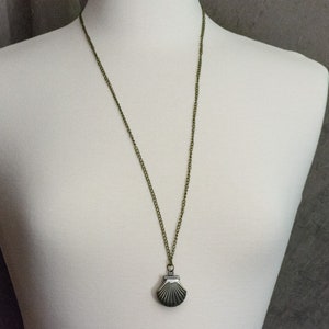 May include: A bronze chain necklace with a silver seashell pendant. The seashell is detailed with lines and has a hinged opening.