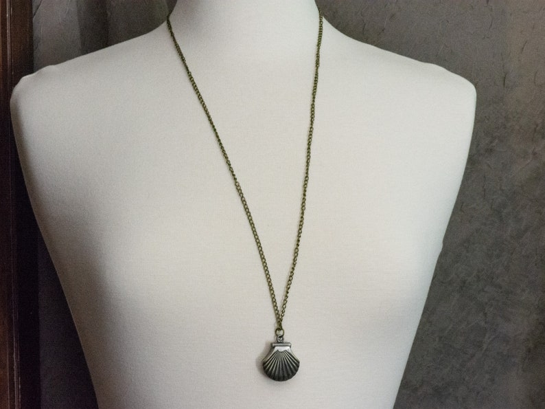 May include: A bronze chain necklace with a silver seashell pendant. The seashell is detailed with lines and has a hinged opening.
