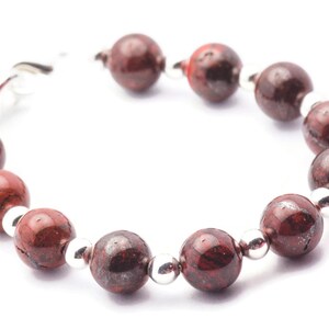 May include: A red and silver beaded bracelet with a clasp fastening. The beads are round and have a speckled pattern.