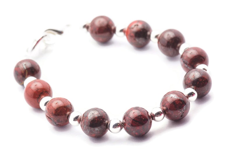May include: A red and silver beaded bracelet with a clasp fastening. The beads are round and have a speckled pattern.
