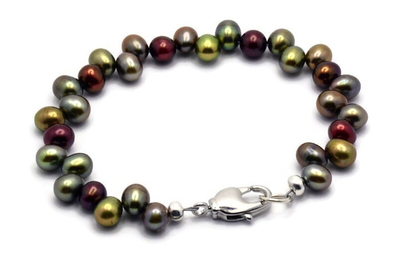 Puede incluir: Un brazalete de perlas multicolores con un cierre plateado. Las perlas son una mezcla de verde, marr&oacute;n y rojo.