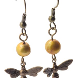 May include: A pair of gold-toned earrings with a single golden pearl and a bee charm on each earring.