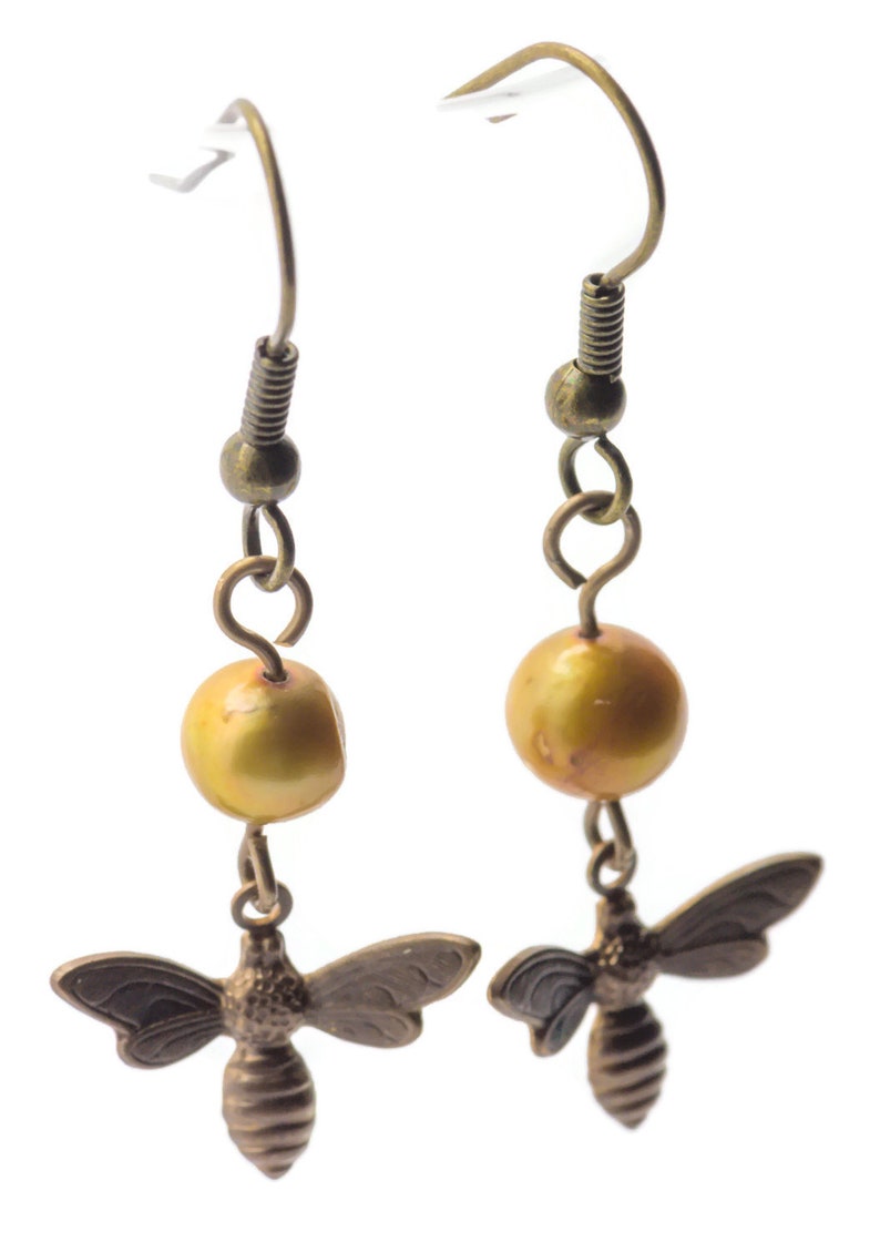 May include: A pair of gold-toned earrings with a single golden pearl and a bee charm on each earring.