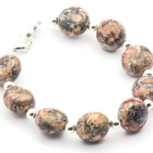 May include: A bracelet made of brown, black, and pink speckled oval-shaped stones with silver accents.