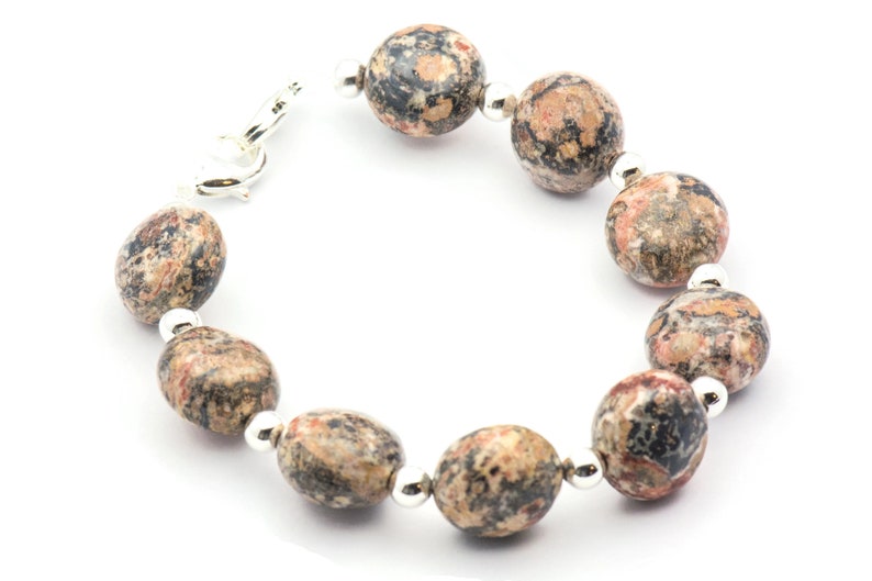 May include: A bracelet made of brown, black, and pink speckled oval-shaped stones with silver accents.