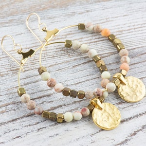 May include: Gold hoop earrings with a hammered gold disc charm and a mix of light brown, beige, and green beads.