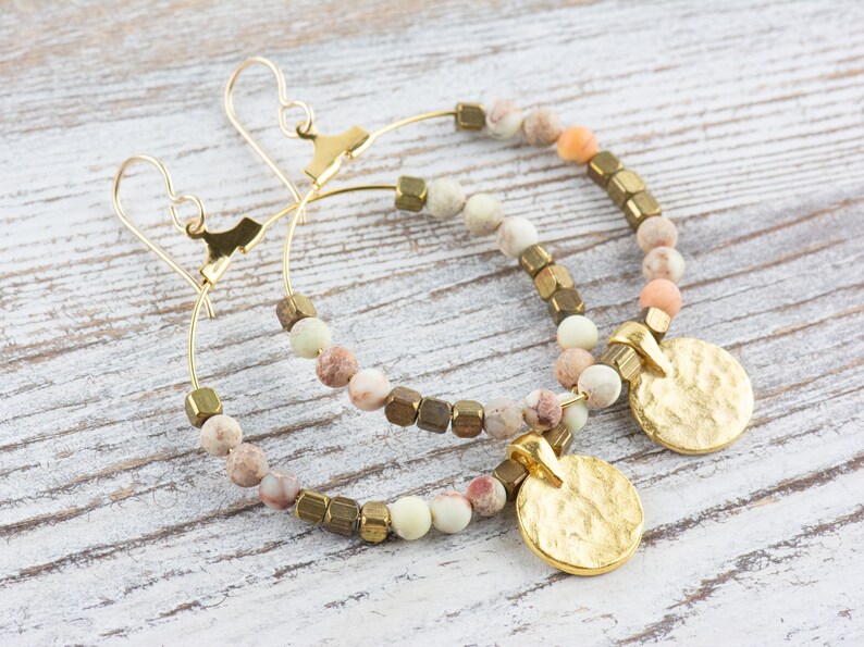 May include: Gold hoop earrings with a hammered gold disc charm and a mix of light brown, beige, and green beads.