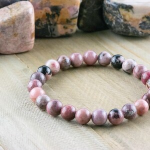 May include: A pink and black gemstone bracelet with round beads. The bracelet is made of natural stones and is a beautiful and unique piece of jewelry.