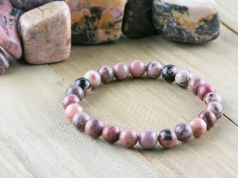 May include: A pink and black gemstone bracelet with round beads. The bracelet is made of natural stones and is a beautiful and unique piece of jewelry.