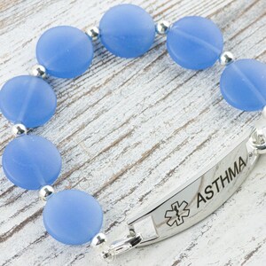 Peut inclure: Un bracelet en perles bleues avec une plaque d'alerte m&eacute;dicale en argent indiquant "ASTHMA" et un symbole d'&eacute;toile de la vie.