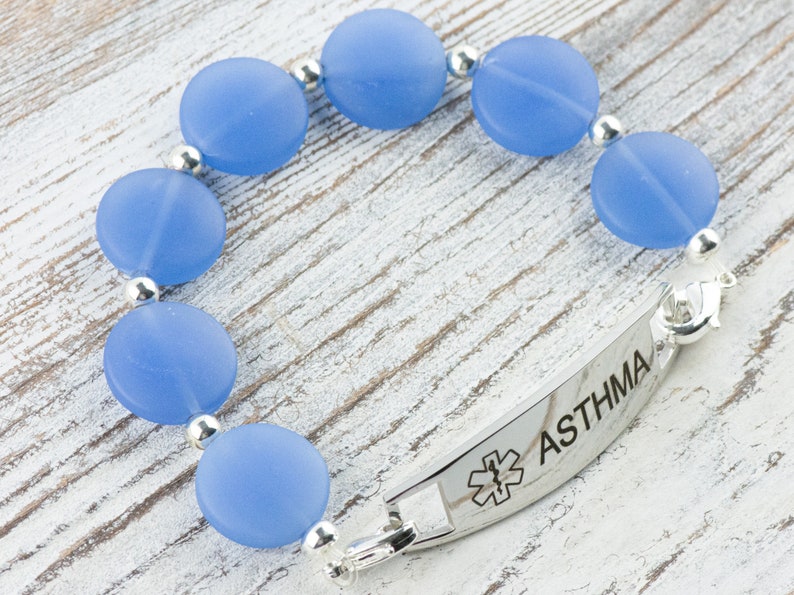 Peut inclure: Un bracelet en perles bleues avec une plaque d'alerte m&eacute;dicale en argent indiquant "ASTHMA" et un symbole d'&eacute;toile de la vie.