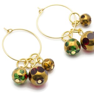 May include: Gold hoop earrings with three dangling charms. The charms are round and have a gold finish with green, red, and brown polka dots.
