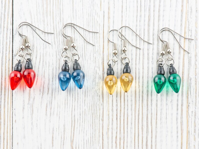 Op de afbeelding: Vier paar hangende oorbellen met lichtbollen in de kleuren rood, blauw, geel en groen. De oorbellen zijn gemaakt met zilverkleurige metalen haakjes.