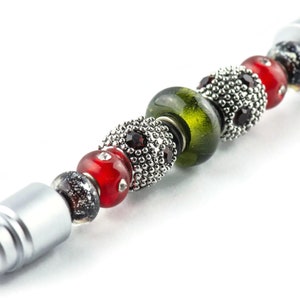 May include: A silver stylus pen with a black rubber tip and a series of colourful beads. The beads are red, green, and black with silver accents.