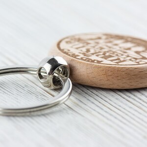 Op de afbeelding: Een houten sleutelhanger met een zilveren ring. Het hout is lichtbruin en de sleutelhanger heeft de tekst "I'm just here for the good times" gegraveerd.