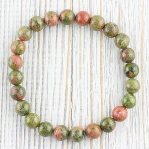 May include: A green, red, and brown speckled stone bracelet with round beads.