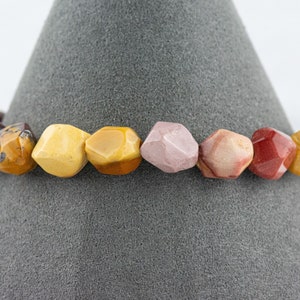 May include: A bracelet made of colorful, faceted gemstone beads. The beads are in shades of red, pink, yellow, and brown.