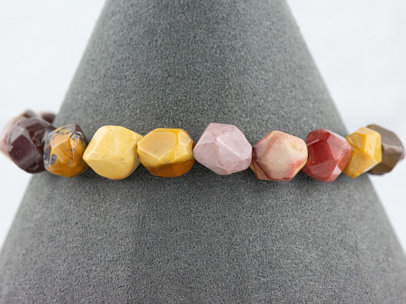 May include: A bracelet made of colorful, faceted gemstone beads. The beads are in shades of red, pink, yellow, and brown.
