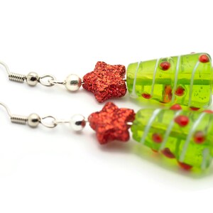 Op de afbeelding: Een paar groene glazen kerstboom oorbellen met rode glittersterren en zilveren haakjes.