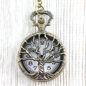 May include: An antique bronze pocket watch featuring a tree of life design. The white watch face has black numerals and hands. The tree design is detailed, and the watch hangs from a matching chain.