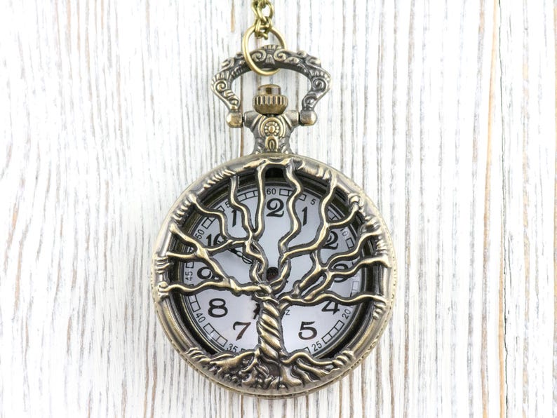 May include: An antique bronze pocket watch featuring a tree of life design. The white watch face has black numerals and hands. The tree design is detailed, and the watch hangs from a matching chain.